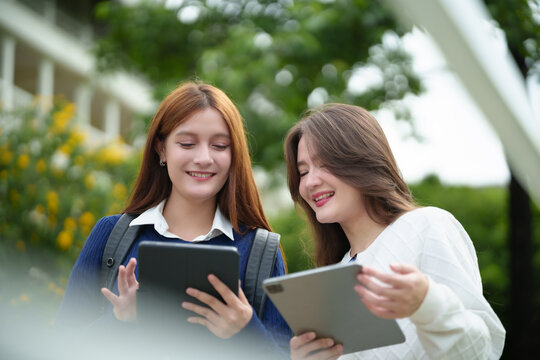 Two college students use digital tablets outdoors, sharing ideas and collaborating on academic work in a modern campus setting.