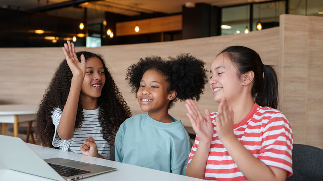 Diverse schoolchildren celebrate teamwork while learning with a laptop in class, reflecting collaboration, digital education, friendship, and positive classroom engagement.