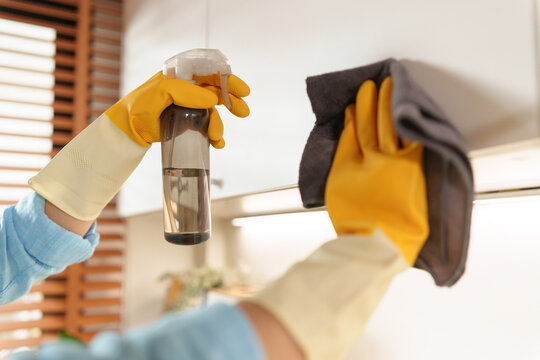 Woman cleans a kitchen cabinet with disinfectant spray and a microfiber cloth, promoting hygiene, sanitation, and efficient household maintenance in a modern home.