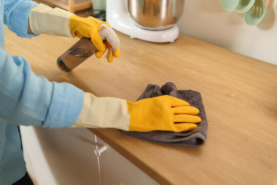 Woman cleans a wooden kitchen countertop with disinfectant spray and a microfiber cloth, promoting hygiene, sanitation, and efficient household cleaning in a modern home.