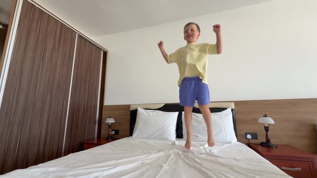 Energetic child enjoying playful jumping in bright modern hotel room. Freedom, happiness, travel lifestyle, comfortable accommodation and joyful family getaway concept.