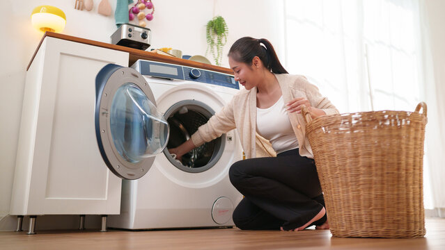 Woman doing laundry with a washing machine in a bright modern home, organizing clothes while promoting cleanliness, convenience, and efficient household care.
