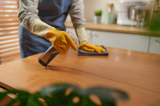Woman sprays cleaner and wipes a wooden countertop with a microfiber cloth, highlighting hygiene, sanitation, and efficient kitchen cleaning in a modern home.
