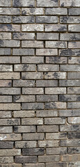 Fototapeta premium Vertical close up of weathered light brown brick surface with variegated colors, exposed aggregate, and mortar gaps where the worn joints have broken away