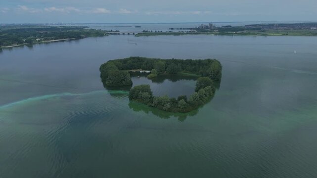 Aerial drone footage circling De Schelp, a small island in Gooimeer in the Netherlands. Scenic view of the island surrounded by water, captured from above with a smooth flying movement.