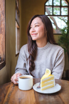 Vertical portrait image of a woman drinking coffee and eating a lemon cake in cafe
