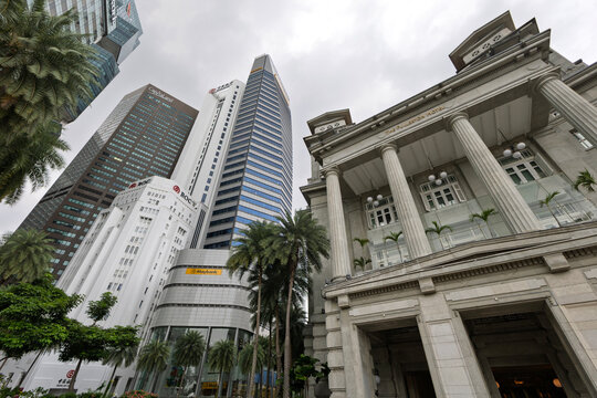 Singapore - Jan 21, 2026: Low-angle view of the historic Fullerton Hotel&rsquo;s neoclassical facade with modern central business district skyscrapers towering behind under a cloudy sky.