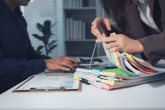 Office Collaboration: Two colleagues are deeply engrossed in paperwork at a desk, surrounded by files and folders, signifying a busy and productive work environment.