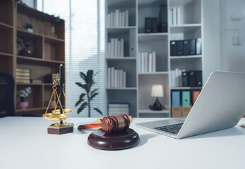 Justice and Law Office: A professional law office setting featuring a gavel, scales of justice, and a laptop on a desk, with bookshelves filled with legal volumes in the background. © Kritdanai