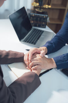 A Moment of Legal Support: Two individuals, one presumably a legal professional, clasp hands in a gesture of solidarity and reassurance in an office setting.