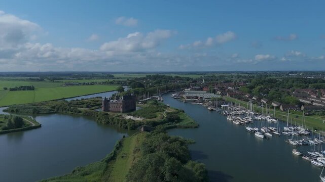 Drone view from a distance over the harbor, castle and village of Muiden, moving from right to left while ascending on a clear day.
