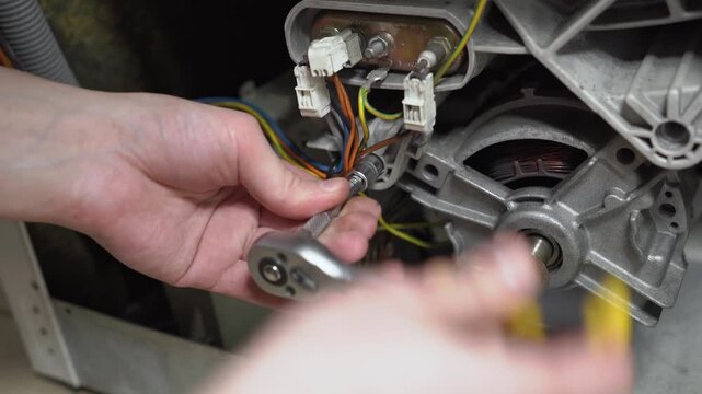 Professional repairman using a socket ratchet wrench to repair the electric motor and wiring of a disassembled washing machine.