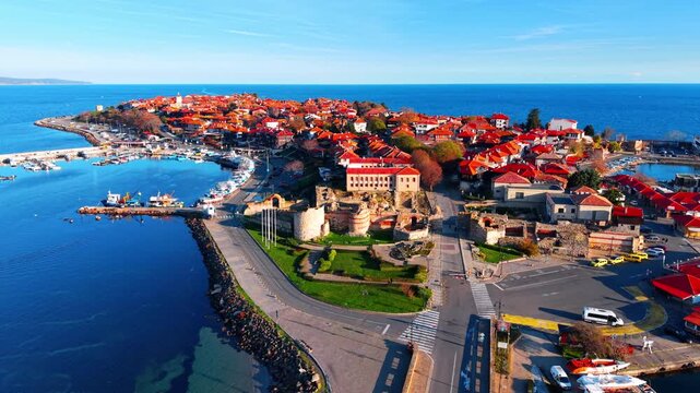 Aerial view of Nessebar old town peninsula, Bulgaria. Red roofed houses, ancient ruins and harbor boats surrounded by clear blue sea.