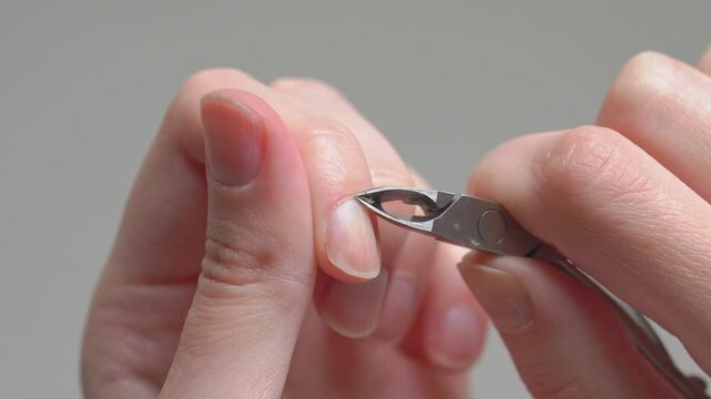 Woman cutting cuticles with professional metal nippers during a home manicure routine, focusing on precise nail care hygiene and beauty processing.	
