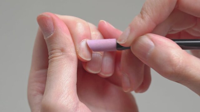 Close-up of a woman doing a DIY home manicure, gently pushing back cuticles with a ceramic stone cuticle remover tool for clean, neat natural nails.	
