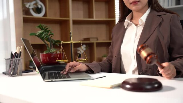 Lawyer Working in Office: A female lawyer in a formal suit works diligently on her laptop in an office setting, holding a gavel in her hand. Representing justice, legal profession.