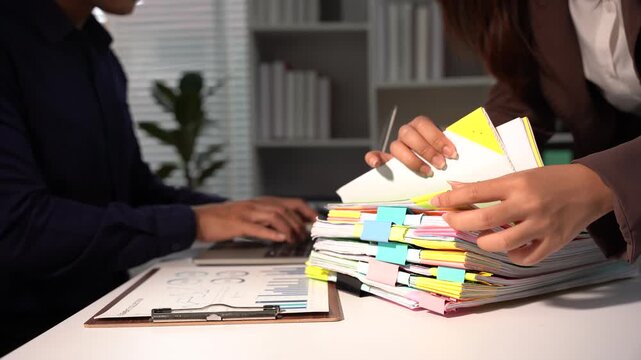 Paperwork Overload: Two business professionals are engrossed in a mountain of documents, highlighting the demanding nature of administrative tasks and workflow management.