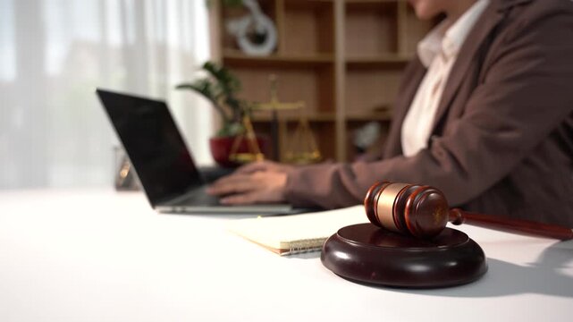 Lawyer Working on Laptop at Desk with Gavel: A focused legal professional is seen working diligently on a laptop at a well-organized desk, with a judge's gavel prominently displayed in the foreground.