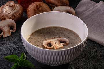 Fototapeta premium Creamy mushroom soup in textured white bowl with fresh mushrooms and basil on dark surface