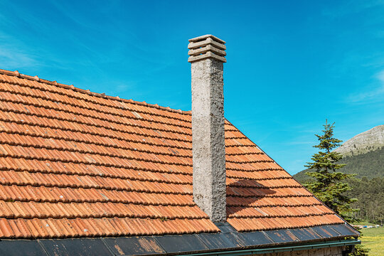 Chimney rising from a traditional clay tiled roof offering shelter in a rural setting with mountains and pine trees