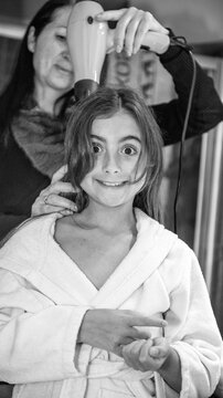 Mother drying daughter's hair with hair dryer at home after bath