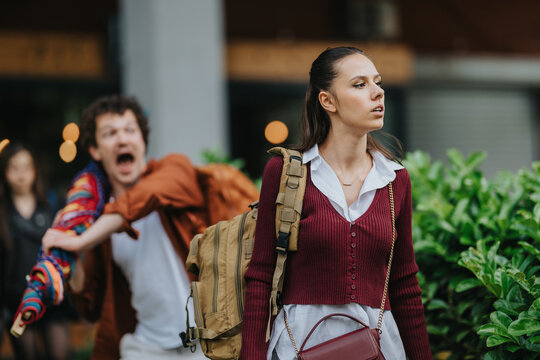 A teenage girl walks away from a classmate while other high school students look on. The scene shows a student being shouted at and a peer reaching toward her in a public outdoor setting.