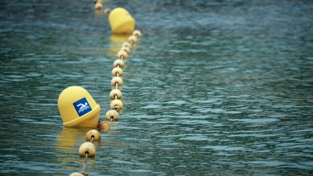 Yellow buoys with a swimming icon floating on water, marking a safe beach swimming area. Ripples visible on water surface