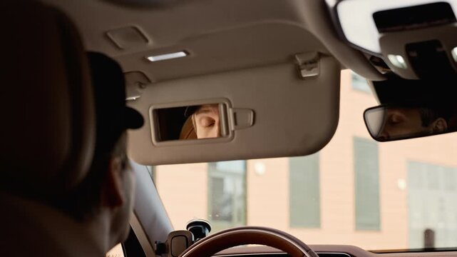 Caucasian middle aged chauffeur adjusting face while looking in car sun visor mirror after removing sunglasses. Ideal for luxury automotive or executive lifestyle marketing campaigns