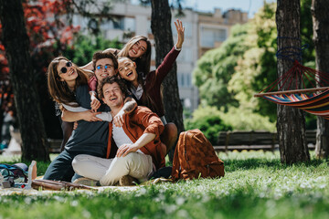 A group of high school students laugh and hug while sitting on a picnic blanket in a park. The young friends pose happily together near trees and a colorful hammock for a relaxed outdoor moment.