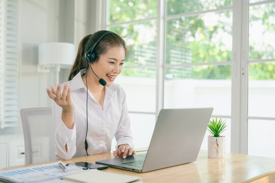 A smiling Asian female call center agent wearing a headset and speaking with a customer, set against an office background.