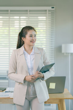 Confident Asian businesswoman standing at office desk and working on digital tablet.