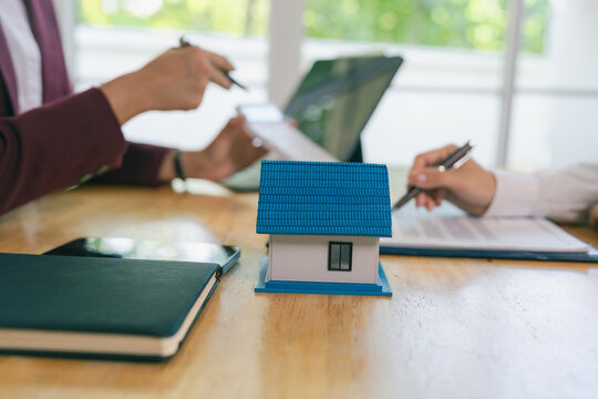 An Asian female client is signing a real estate purchase agreement with an agent who is explaining the contract details to the homebuyer.