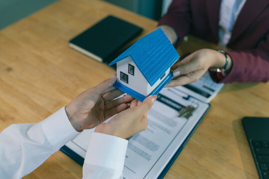 An Asian female client is signing a real estate purchase agreement with an agent who is explaining the contract details to the homebuyer.