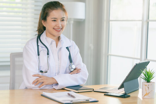 Smiling Asian female doctor sitting at desk with stethoscope in clinic or hospital