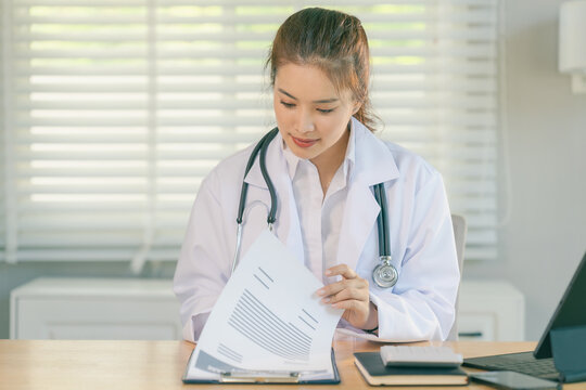 Smiling Asian female doctor sitting at desk with stethoscope in clinic or hospital
