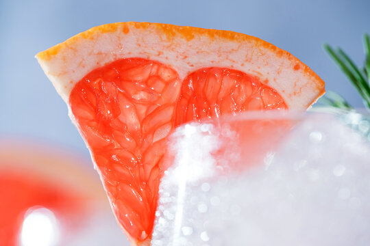 Close-up of a refreshing pink grapefruit cocktail with ice, fresh rosemary, and a juicy grapefruit wedge garnish.Vibrant macro food photography, restaurant menus, cocktail bars, healthy beverages