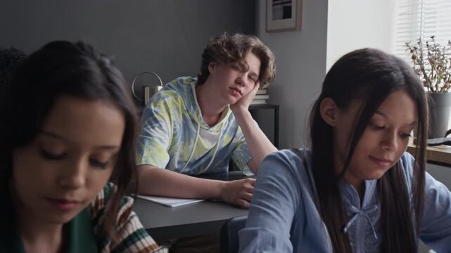 Caucasian teenage boy yawning and looking bored during school lesson while girls sitting in foreground. Perfect for educational marketing and student mental health campaigns