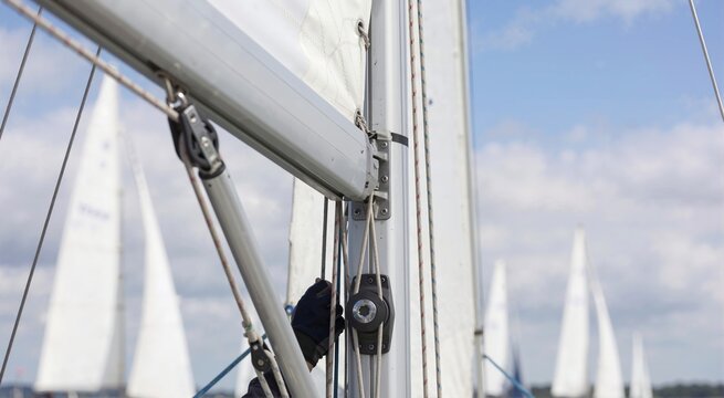 Close up of sailboat mast and rigging with a gloved hand pulling a rope. Sailor adjusting sails during a regatta. Nautical sports and yachting concept