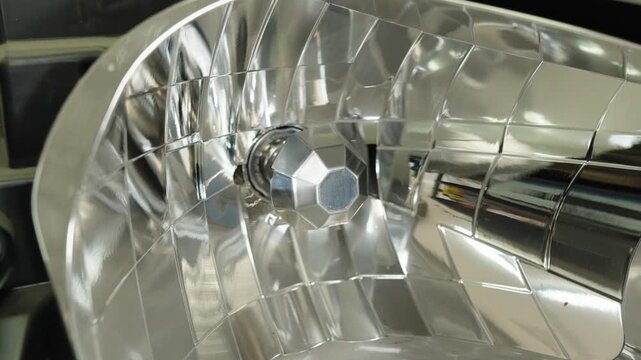 A shiny chrome reflector inside a disassembled car headlight close up.