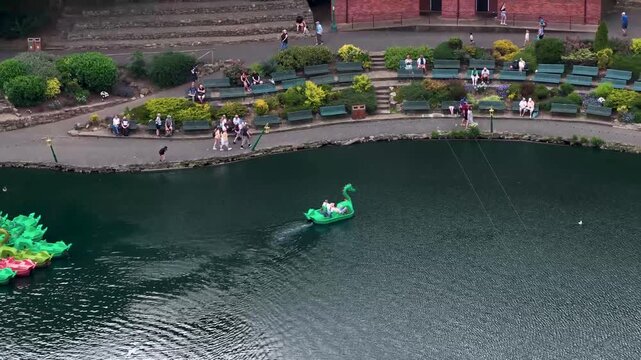 Aerial footage of visitors enjoying a dragon pedal boat on Peasholm Park boating lake with landscaped gardens and lakeside walkways in the popular seaside town of Scarborough North Yorkshire England