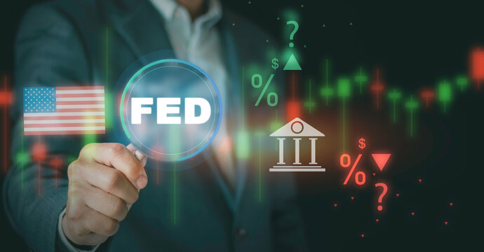 Businessman holding magnifying glass analyzing FED icons with USA flag. Concept of Federal Reserve adjusting interest rates, inflation control, and global economic impact on stock market growth.