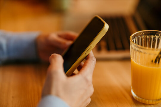 Person hands typing on smartphone with orange juice