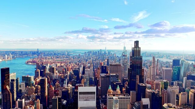 Elevated view of Manhattan skyline with East River, New York. Dense towers stretch toward the horizon under a soft blue sky with scattered clouds.