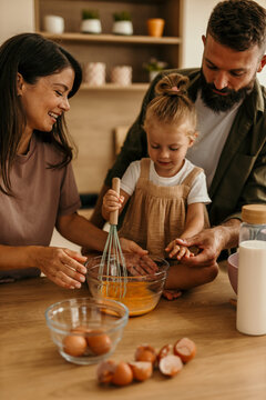 Family cooking together, daughter whisking eggs in kitchen
