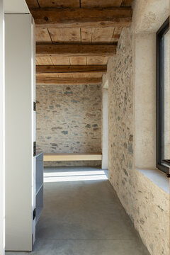 A corridor leading into an empty room with stone walls and a wooden ceiling. A beautiful renovation featuring a polished concrete floor.