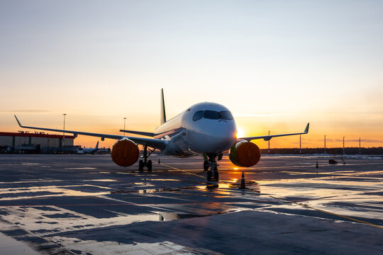 Modern passenger plane on the airport against the backdrop of a picturesque sunrise with reflection in a puddle