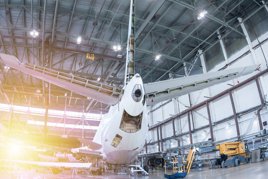 Rear view of white passenger airplane in the aircraft hangar. Plane under maintenance. Checking mechanical systems for flight operations
