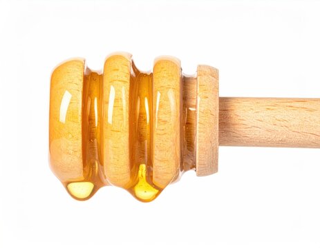 Golden liquid drips from grooved wooden dipper on white background