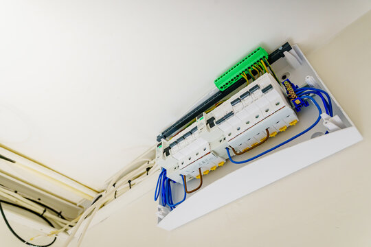 Diagonal low angle view of an open domestic electrical panel with neat wiring, circuit breakers, RCD switches, and grounding block on white wall.