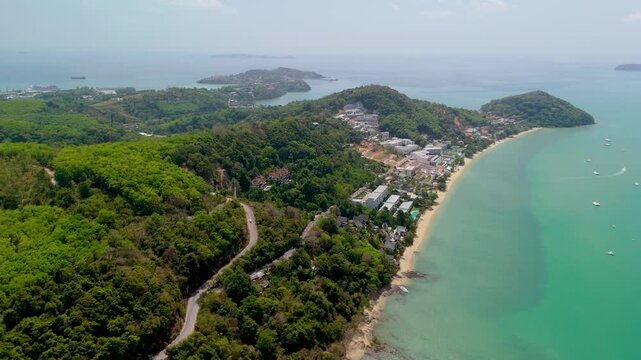 Lush green hills overlook the turquoise ocean waters at Ao Yon Beach in Phuket during a bright and sunny afternoon with small boats sailing near the shore